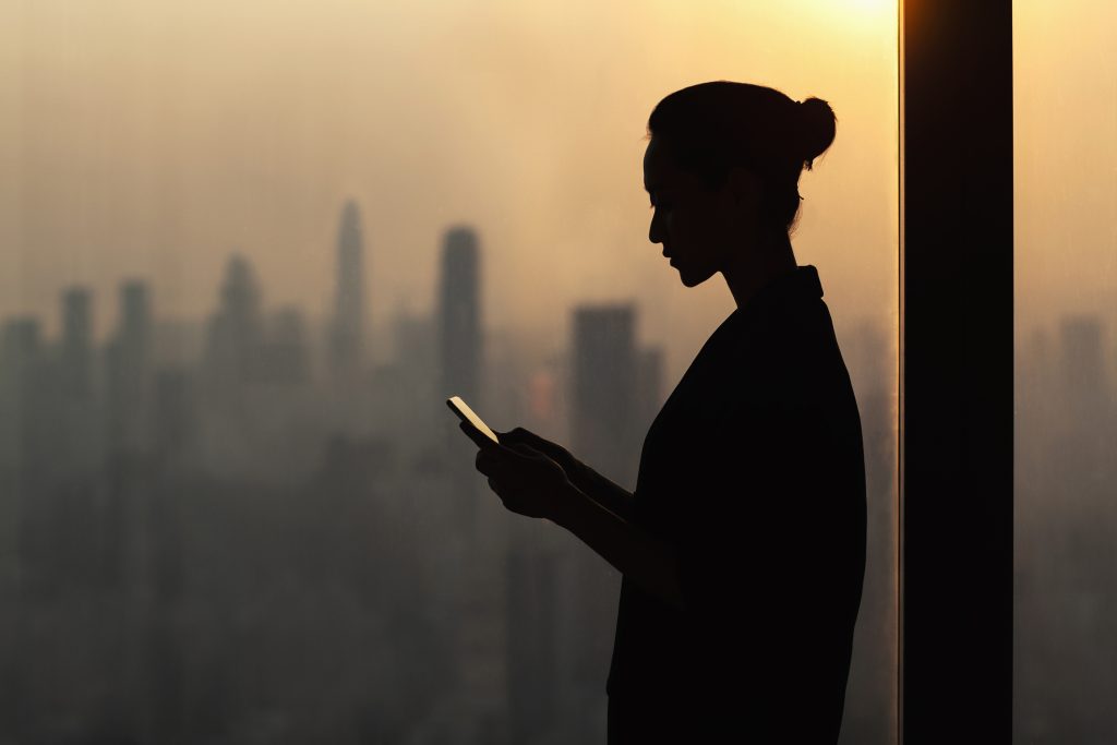 A silhouette of a woman using a cell phone in front of a city.