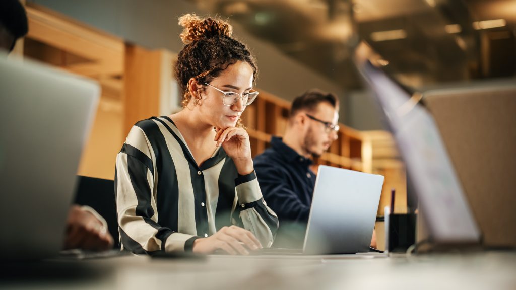 A woman in a striped shirt and glasses looking at a laptop.