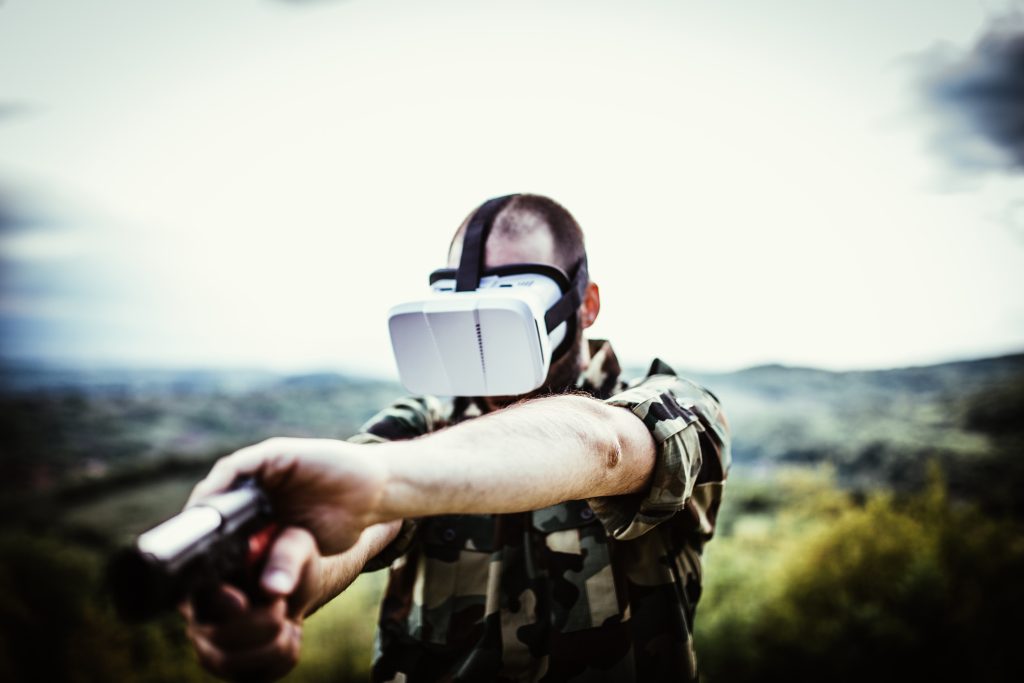 Soldier in the mountain lurking with a gun in his hands, he is wearing a virtual reality headset