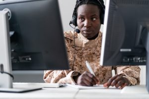 Une femme en uniforme militaire assise à un bureau avec deux ordinateurs.