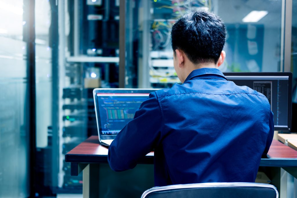 A man working on a laptop in a server room.