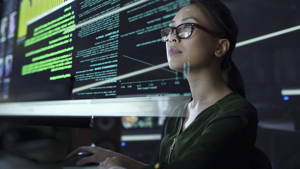 A woman in glasses is looking at a computer screen.