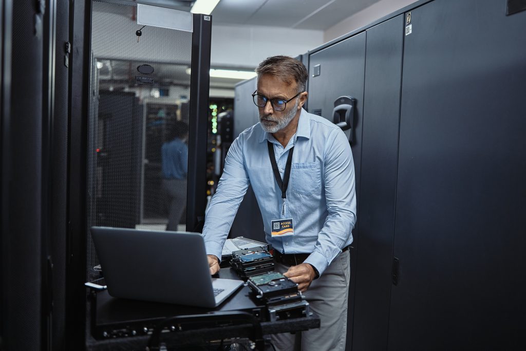 A man working on a laptop in a server room.