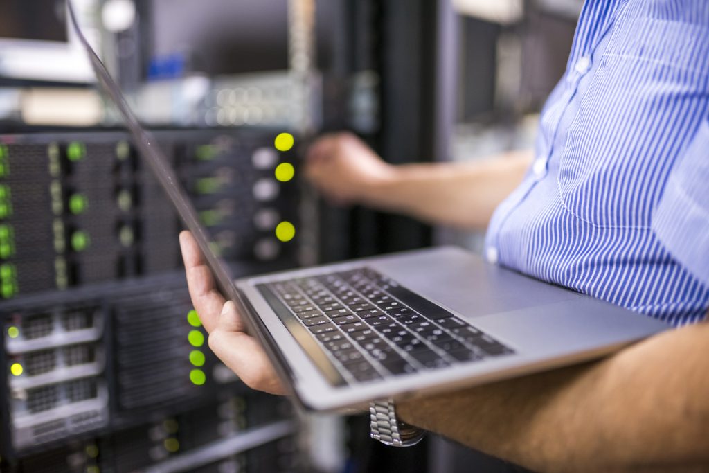 A man holding a laptop in a server room.