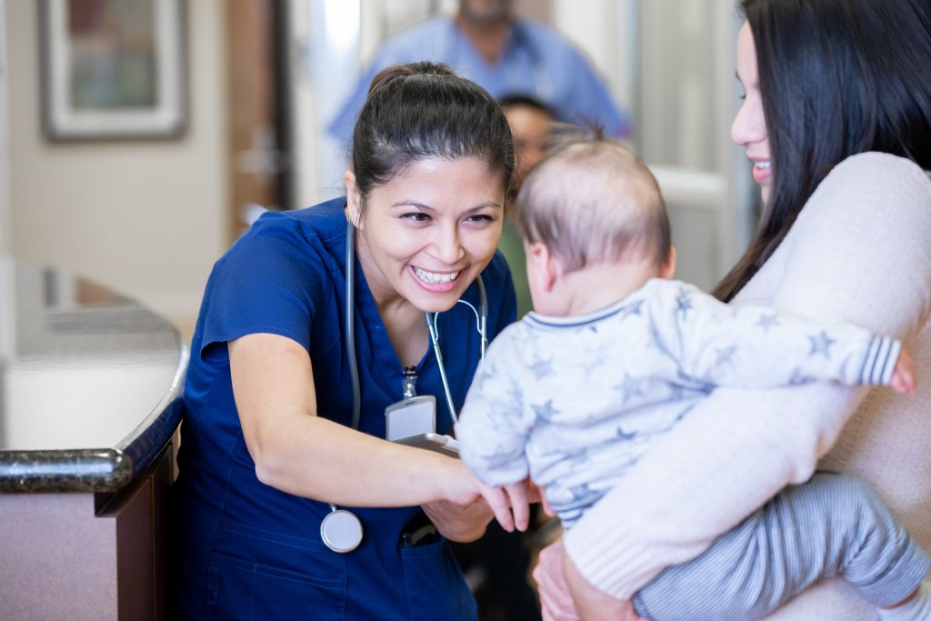 Healthcare professional smiling at a baby held by a mother.