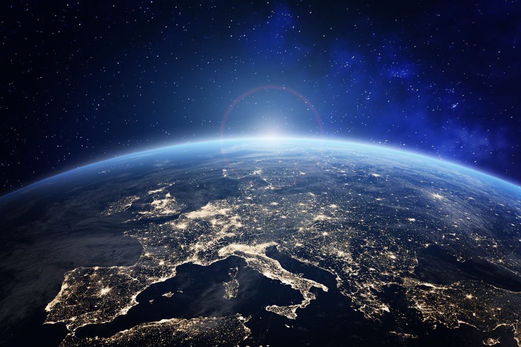 The earth at night with the sun shining on it.